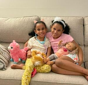 Two young girls sitting on a couch with dolls in their laps