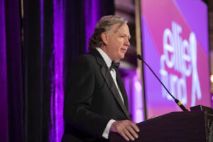 Man in a tuxedo speaking at a podium