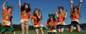 Six young girls in matching orange shirts jumping in the air at the same time